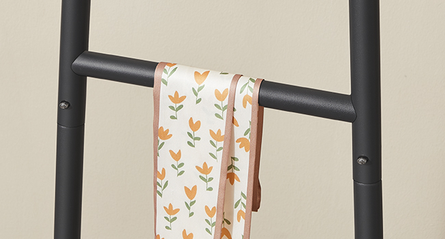 Közeli kép egy fekete fém létra stílusú állványról, virágmintás anyaggal a létrafok felett, valószínűleg törölköző vagy ruha kiállítására.