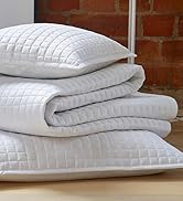 Stack of white quilted bedding items including pillow and comforter. Textured surface visible on all pieces.