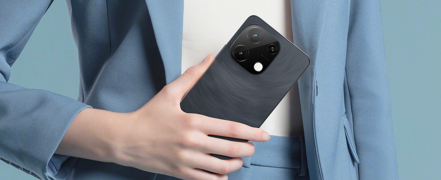 Black smartphone with square camera module being held against blue fabric background, showcasing slim profile and matte finish.