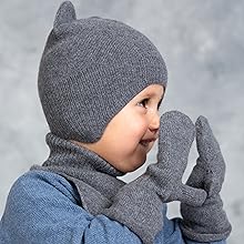 Child wearing grey winter hat and matching mittens with blue coat, demonstrating winter accessories against grey background.