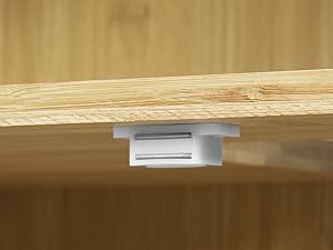 Close-up of a white plastic bracket attached to the underside of a light wooden surface, likely for securing or organizing cables.