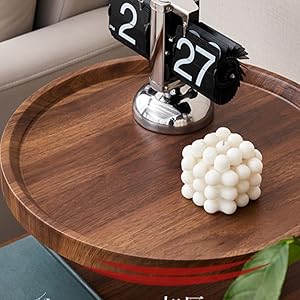 Round wooden decorative table surface displaying a digital clock, decorative white sphere, and book against neutral background.