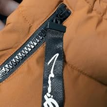 Close-up of a zipper on a tan-colored garment. A black fabric tag with white text is visible next to the zipper.
