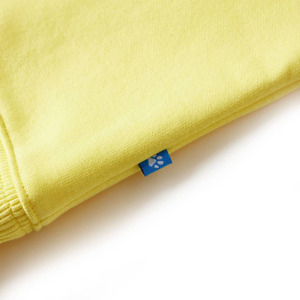 Close-up of a yellow fabric garment corner, showing a small blue tag with white stitching attached to the seam.