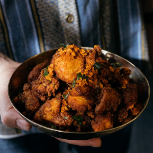 CHETTINAD CHICKEN BITES in a metal bowl with hands cupped around it