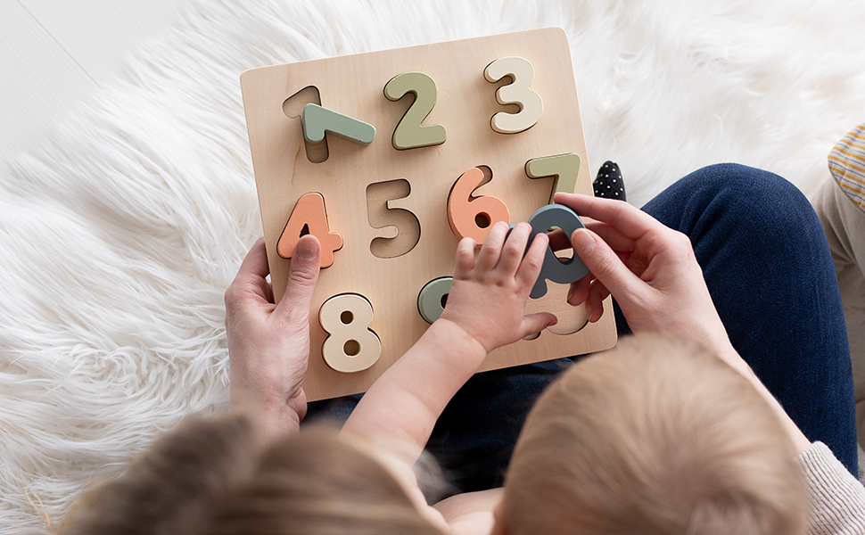 Young child and mom playing with wooden numbers puzzle on the floor