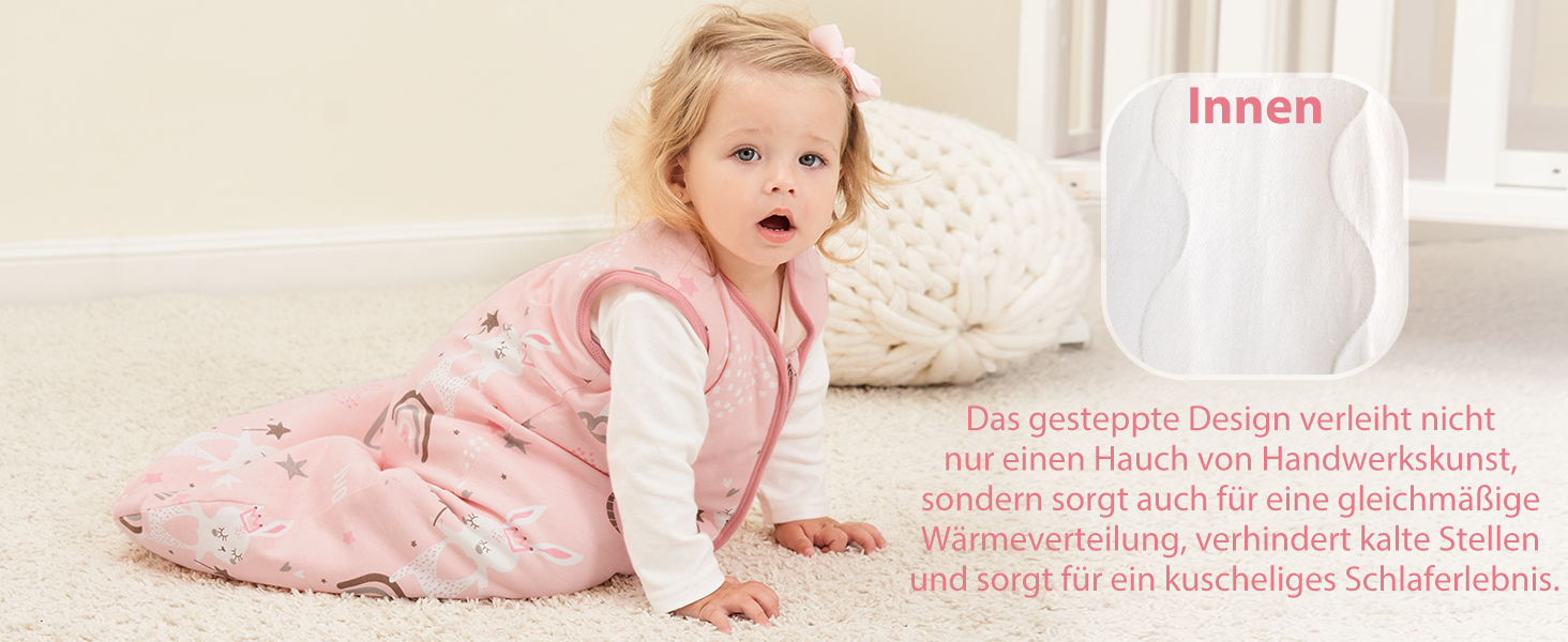 Säugling in rosafarbenem Schlafanzug mit weißen Ärmeln, das auf hellem Boden krabbelt. Strukturiertes weißes Kissen