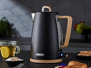 Modern black electric kettle with wooden handle photographed against dark background, shown with food and beverage items.