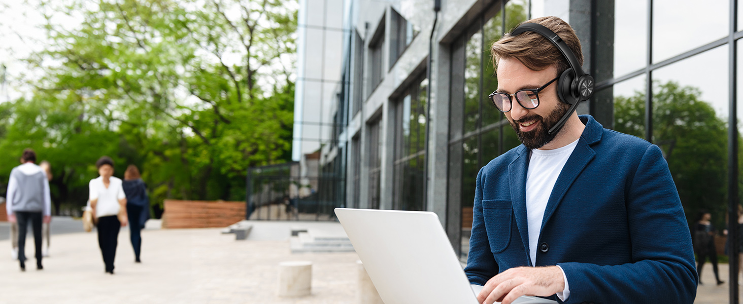 Professional wearing a navy blazer, white t-shirt, and wireless headset standing in a modern office exterior setting with glass windows.