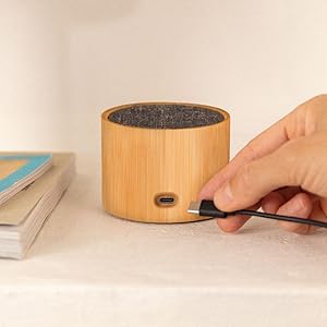 Altavoz cilíndrico de bambú o madera con superficie superior oscura, que se muestra en una superficie de color claro con controles de ajuste manual