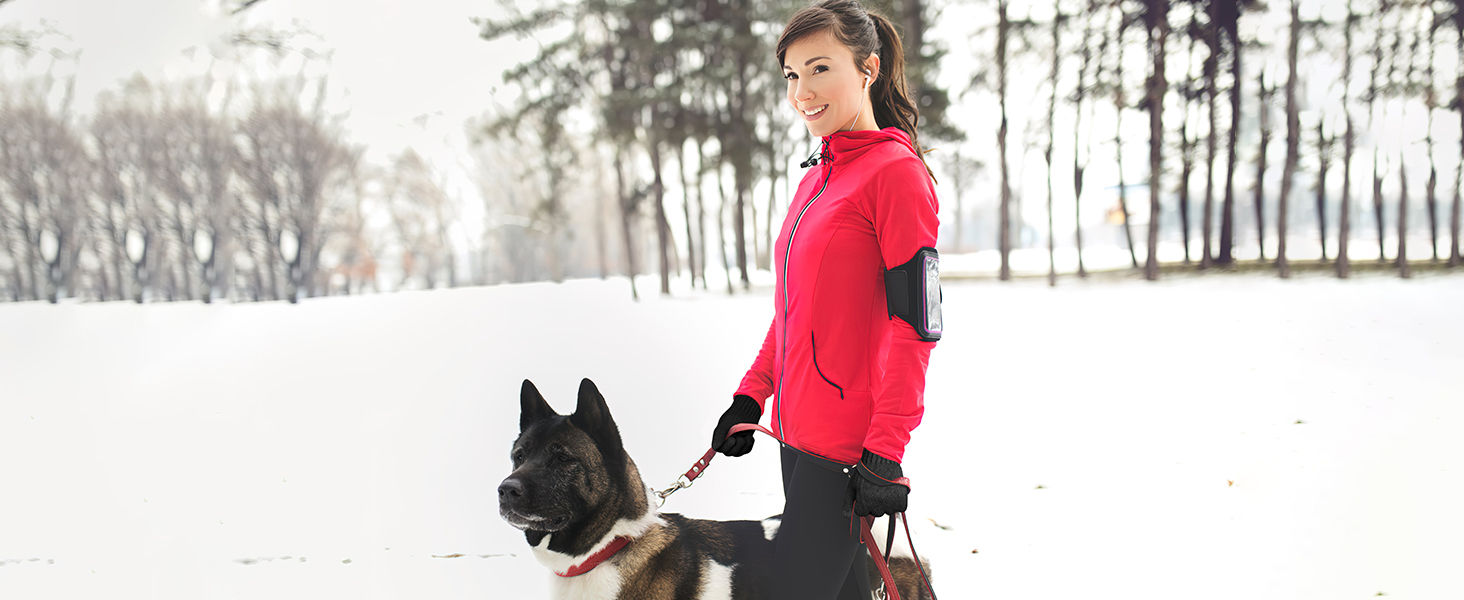 Person in bright red jacket walking a black dog through a snowy forest landscape.