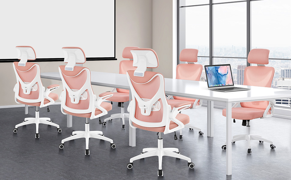 Modern office space with pink ergonomic chairs. White desks, large windows, and a laptop visible. Chairs feature mesh backs and adjustable armrests.
