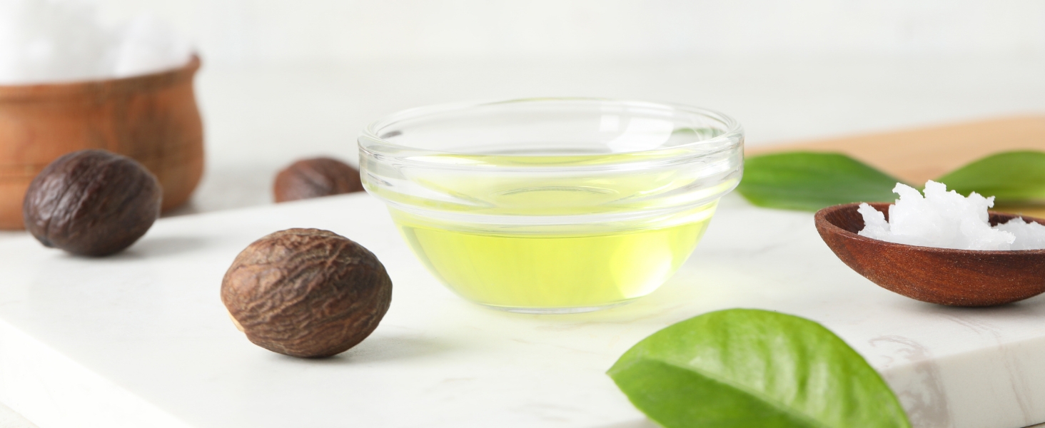 plant-based oil, surrounded whole nuts, green leaves, and a wooden spoon with white coconut flakes