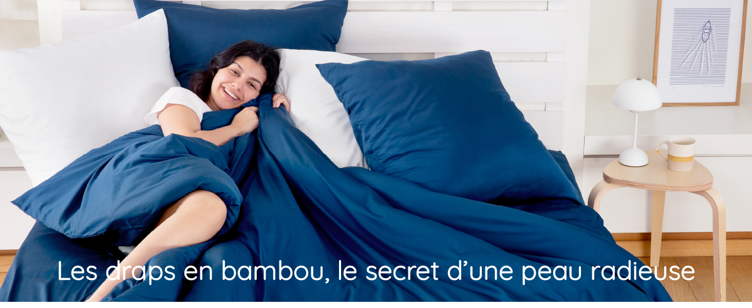 femme souriante et radieuse dans un lit avec une housse de couette bleu marine
