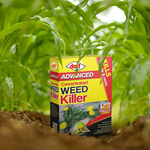 Yellow box of Doff Advanced Concentrated Weed Killer placed on soil, surrounded by green grass or plant leaves. Product promises to kill weeds.