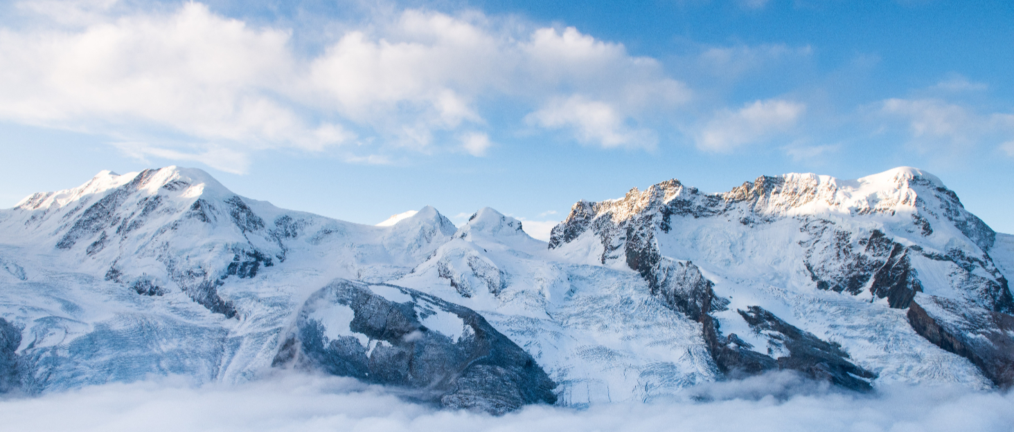 Secuencia panorámica de picos montañosos cubiertos de nieve contra el cielo azul, que muestra una cadena montañosa continua con glaciares y laderas blancas.