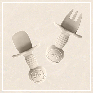 Two white silicone utensils with screw-like bases and smiling face designs. One has a spoon-shaped end, the other a fork-shaped end.