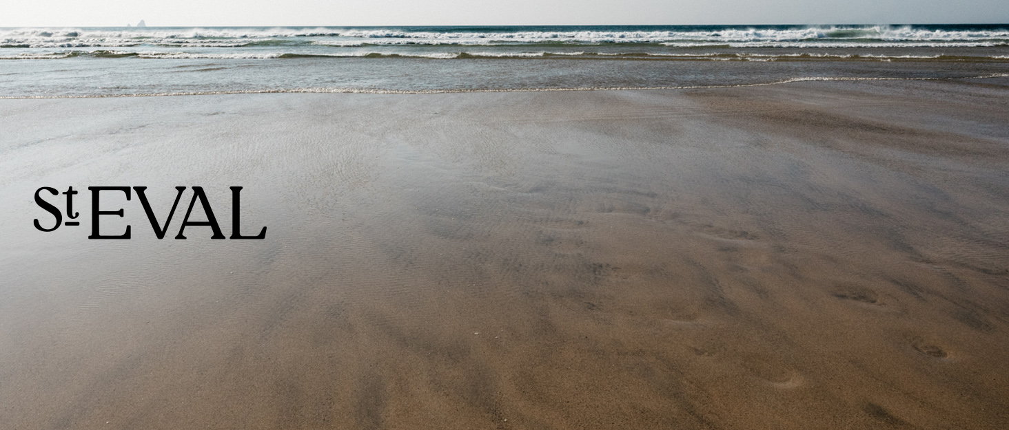 Sandy beach with gentle waves in the distance. The text 'St EVAL' is visible in the foreground, partially obscured by sand.