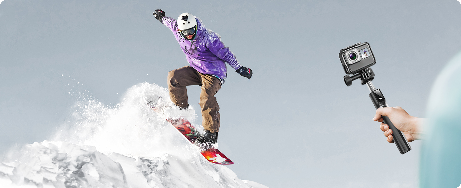 Snowboarder in purple jacket performing mid-air jump on snowy slope. Action camera on selfie stick visible in foreground, capturing the moment.