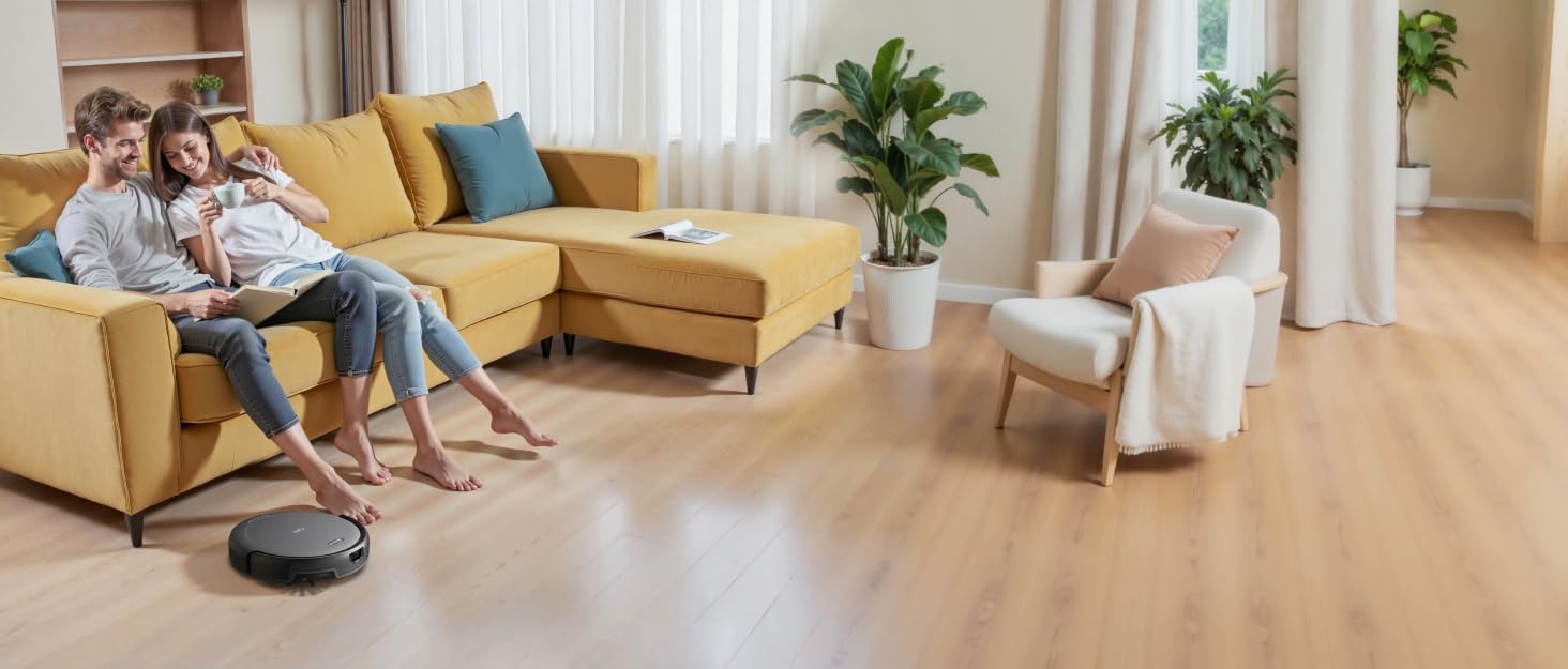 Runder Roboterstaubsauger auf Holzboden im Wohnzimmer mit gelbem Ecksofa, Sessel und Topfpflanzen. Das Gerät wird in Gebrauch gezeigt