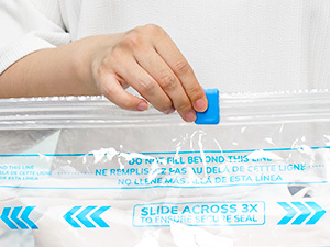 Gros plan des mains manœuvrant un sac de rangement en plastique muni d'un mécanisme de fermeture coulissant bleu et d'instructions imprimées