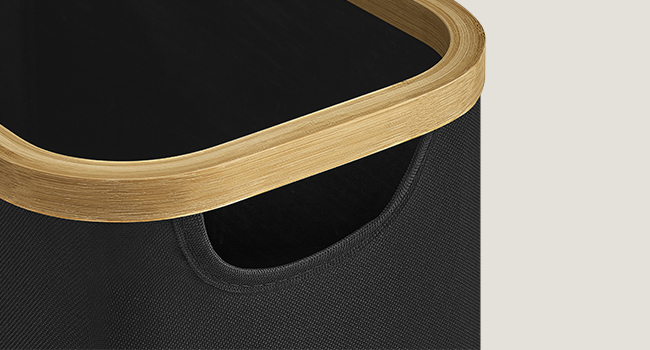 Közeli kép egy fekete, ívelt fa peremű tartályról. A tartály texturált felülettel és kivágott fogantyúval rendelkezik az oldalán.