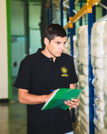 Lagerarbeiter im schwarzen Poloshirt überprüft Dokumente auf dem Klemmbrett zwischen Lagerregalen und Industrieregalen.