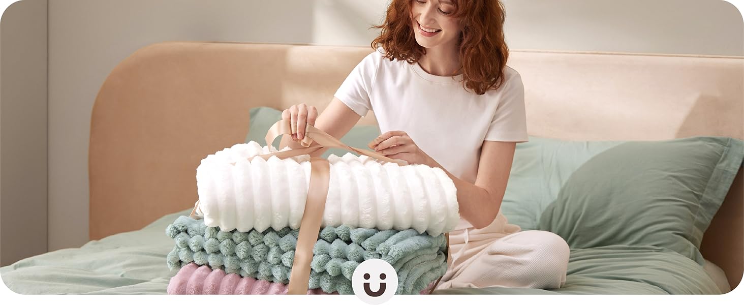 Stacked colorful textured pillows on a bed, with hands arranging them. Pillows have varied patterns and textures, creating a layered, decorative effect.