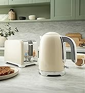 Modern electric kettle in cream/off-white color positioned on kitchen counter with bread and decorative elements in background.