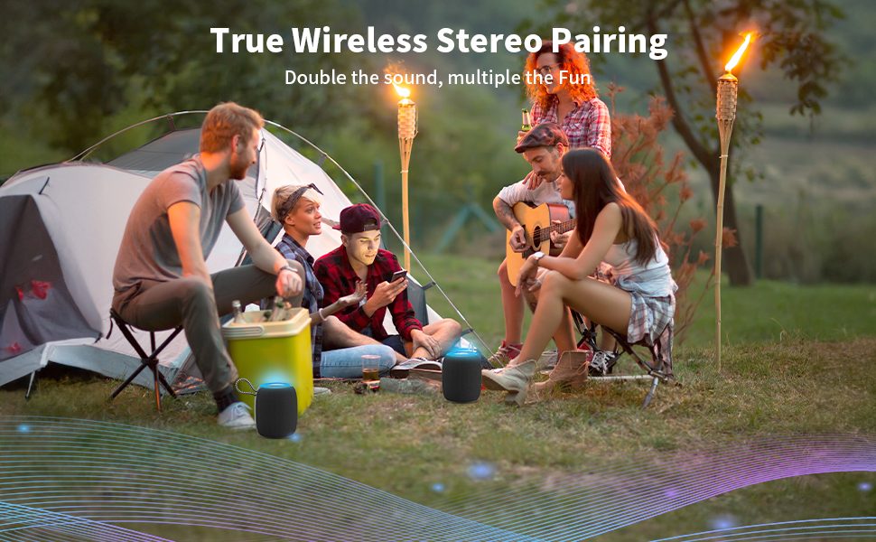 Outdoor camping scene showcasing wireless stereo pairing feature, with portable speakers visible near a tent and tiki torches at dusk.