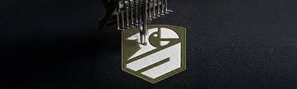 A close-up of a sewing machine needle embroidering a geometric bird design on dark fabric