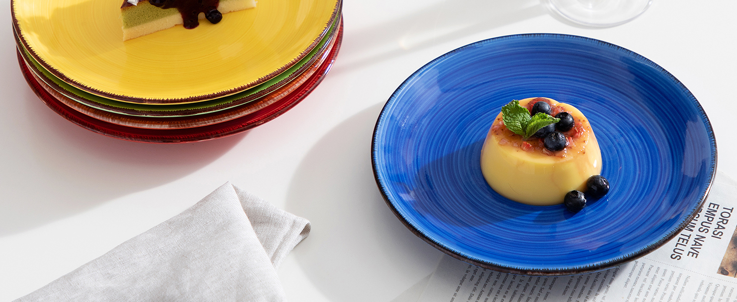 Series of colorful ceramic plates in yellow, red, and blue, each featuring elegant food presentation with garnishes.