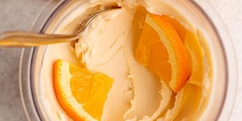 reamy orange ice cream in a Ninja CREAMi container, garnished with fresh orange slices.