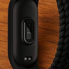 Close-up of black plastic device with button or switch interface mounted on braided black rope or cord against wooden surface.