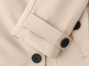 Primo piano in tessuto beige con due grandi bottoni neri, probabilmente parte della manica di un cappotto o di una giacca
