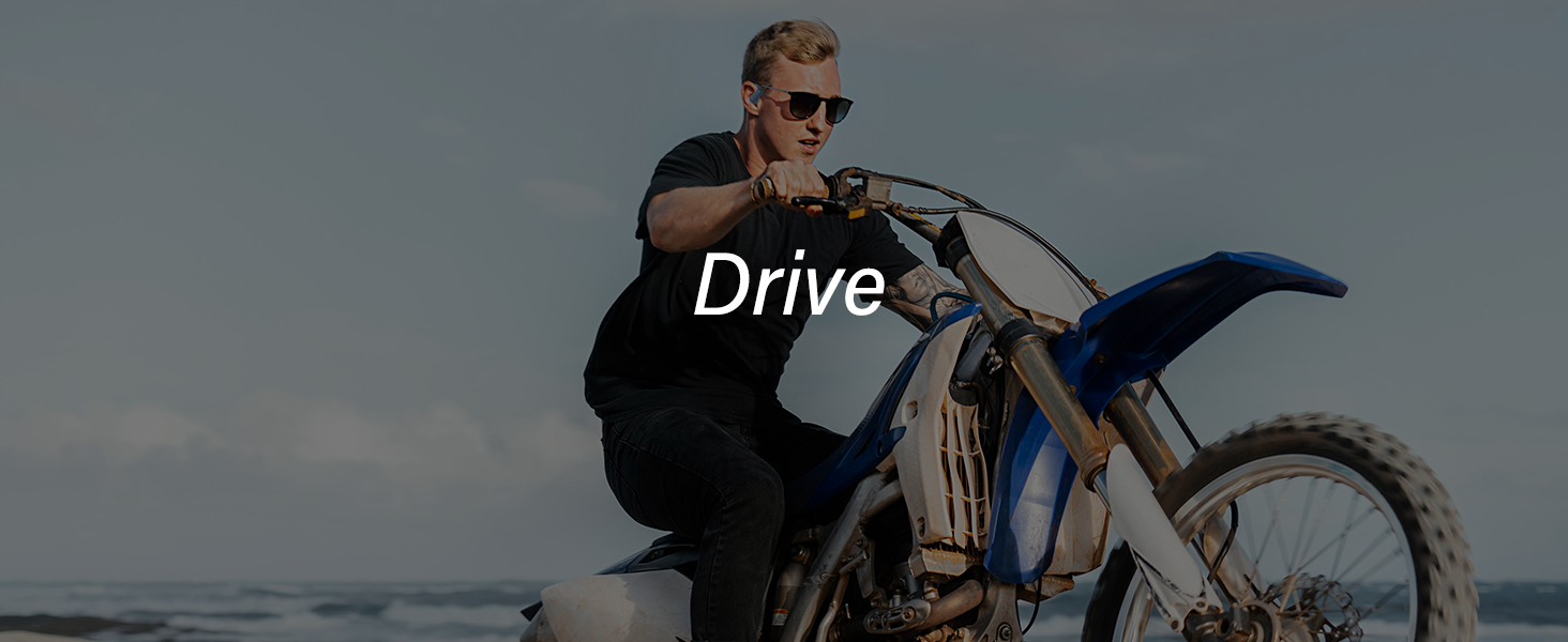 Person wearing sunglasses riding a blue and silver off-road motorcycle on a beach. The word 'Drive' is overlaid on the image.