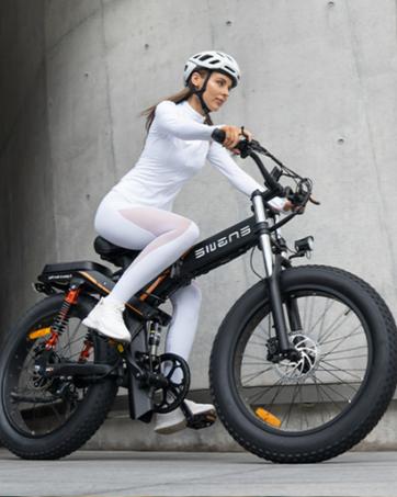 Electric bike with fat tires and 'SWAGTRON' branding on frame. Rider demonstrates use, wearing white outfit and helmet against concrete wall.