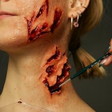 makeup artist applying alcohol drying blood with brush on woman&#39;s neck with prosthetics