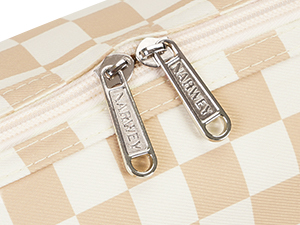 Close-up of metallic zipper pulls on a cream and beige checkered pattern surface, showing detailed hardware construction.