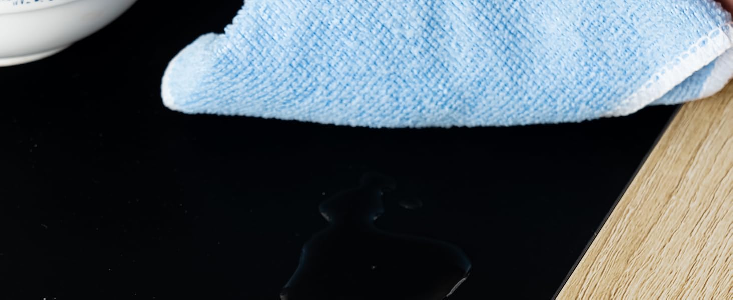 Eine blau-weiße Porzellanteekanne mit einem hellblauen Mikrofasertuch auf einer schwarzen Oberfläche von Hand abwischen