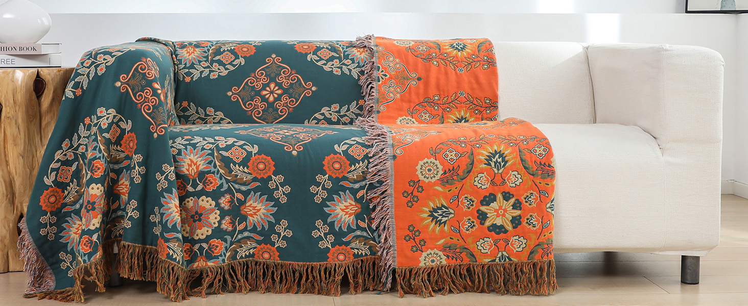 Decorative throw blanket with floral patterns in teal and orange, featuring fringed edges, draped over a white couch.