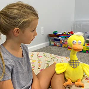 una niña sentada en una cama con un pato amarillo de juguete.