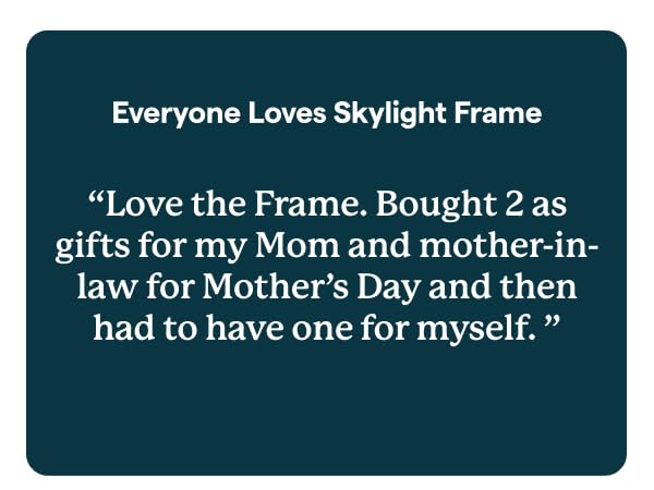 Skylight digital photo frame on table, with hand holding phone.