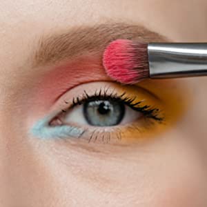 que aplica una sombra de ojos rosa vibrante en los párpados, con sombras de ojos amarillas y azules visibles. Primer plano del ojo