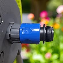 Close-up of blue connector or adaptor piece attached to black equipment, with colorful garden flowers blurred in background.