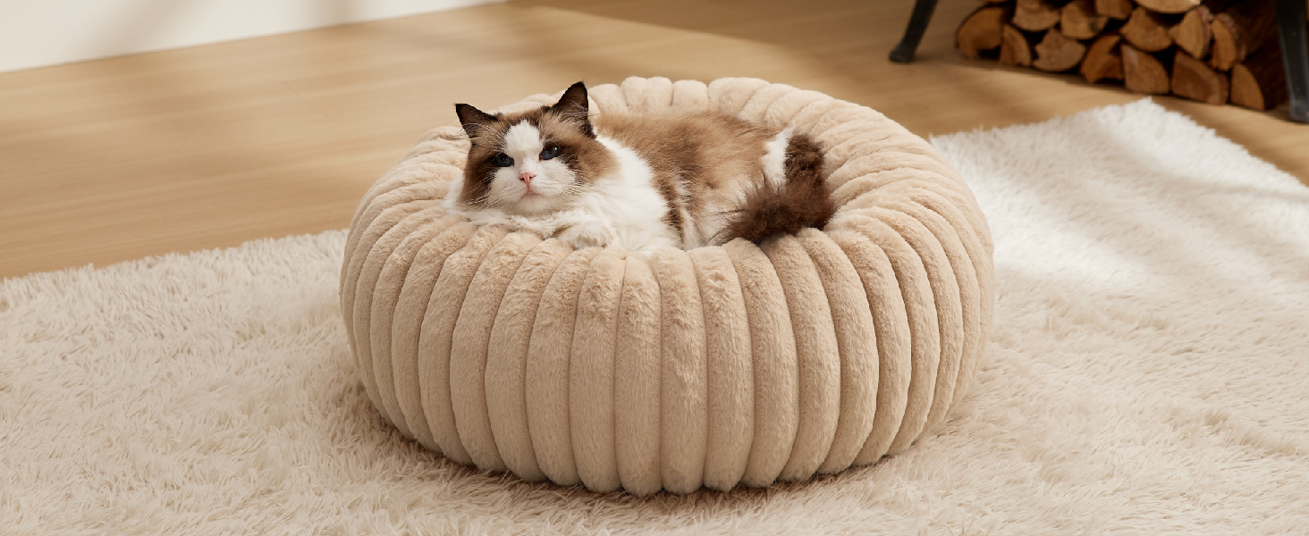 Rundes, geripptes Hundebett in beige Farbe mit einer siamesischen Katze, die darin ruht. Das Bett sieht plüschig aus, ist gepolstert und hat ein kreisförmiges Design.