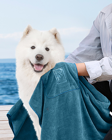 PETTOM 2 Pcs Dog Towel Quick Drying Absorbent Microfiber Dog Towel Artero, Bath Towels with Pockets for Small, Medium and Large Dogs, 90 x 50 cm 17 Perro blanco y esponjoso en la cubierta del barco con una persona sosteniendo una toalla verde azulada. Fondo oceánico visible.