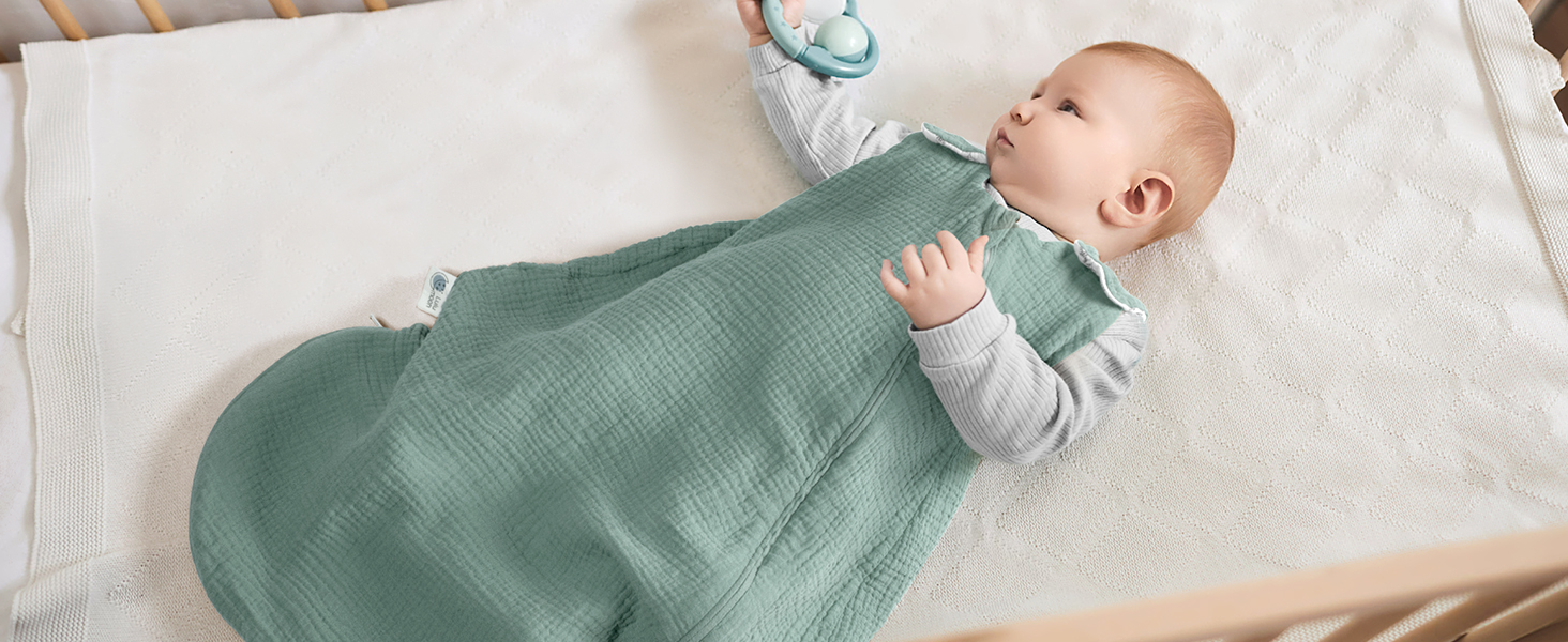 ein Baby in einem grünen Kleid mit einer blau-weiß gestreiften Decke.