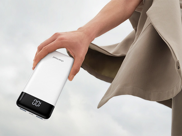 Hand reaching to pick up a black smartphone from gray fabric surface, demonstrating grip or handling motion.