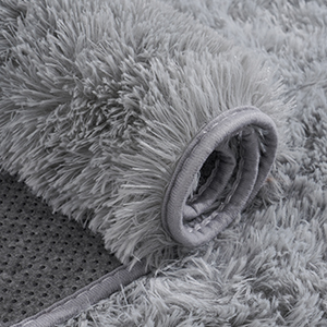 Close-up of a fluffy gray rug or carpet, showing plush texture and a partially visible rolled edge.
